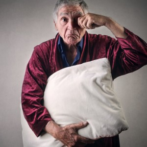 Sleepy elderly man with night-gown holding a pillow
