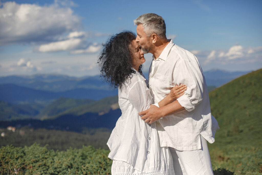 Senior man and woman in the mountains. Adult couple in love at sunset. Man in a white shirt.
